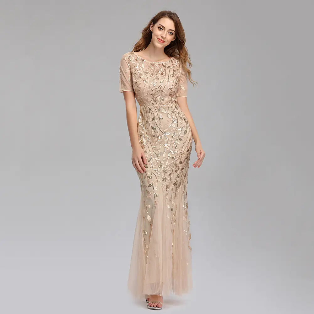 A shimmering champagne-colored embroidered sequin mermaid evening gown with delicate gold leaf embroidery and sheer short sleeves featuring a tulle skirt.