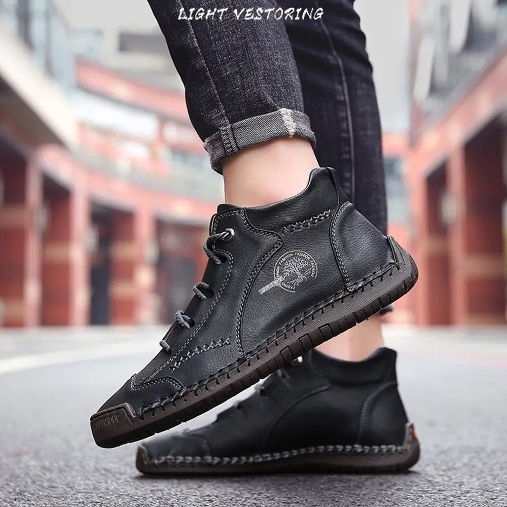 Black leather ankle boots hand stitched with visible stitching and a circular logo on the side designed as vintage high top sneakers.