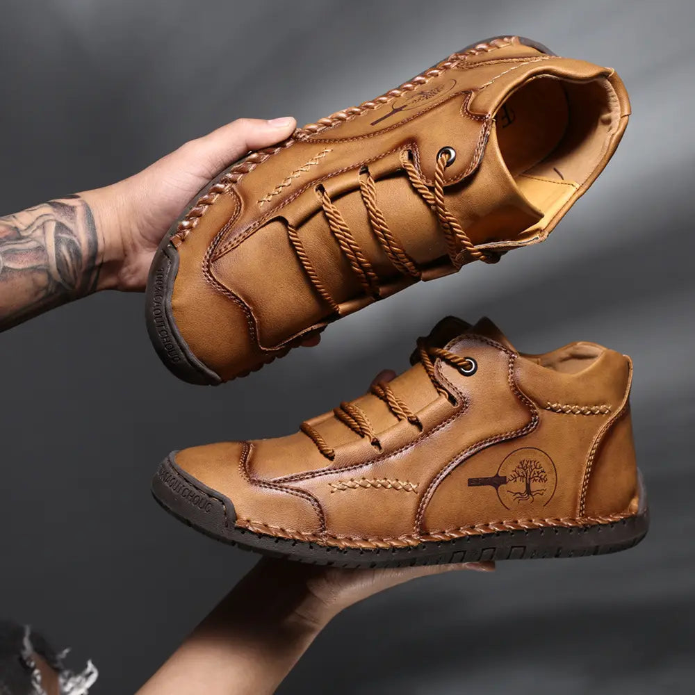 Tan leather hand stitched vintage high top sneakers with braided laces and a tree emblem on the side designed as men’s hiking boots.
