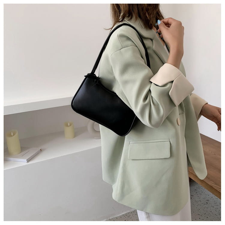 Eine schwarze Schultertasche aus Leder mit elegantem minimalistischen Design und strukturierter rechteckiger Form; sie verfügt über einen gebogenen Unterarmstil aus Kunstleder.