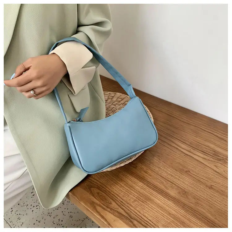Eine hellblaue minimalistische Umhängetasche aus Kunstleder mit gebogenem Unterarmgriff, mit elegantem Design und passendem Riemen.