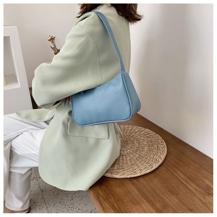 Eine zartpastellblaue minimalistische Umhängetasche aus Kunstleder mit gebogenem Unterarmgriff, mit elegantem Design zur Schulterwendung.