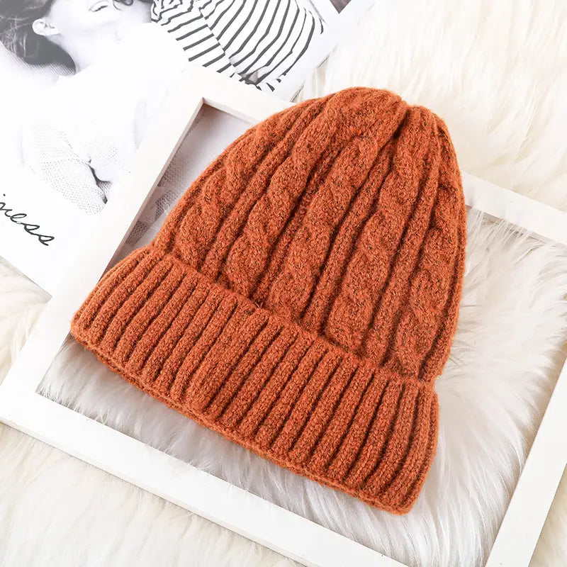 A cozy rust orange cable knit beanie hat with a ribbed cuff and fleece lined interior for winter warmth.