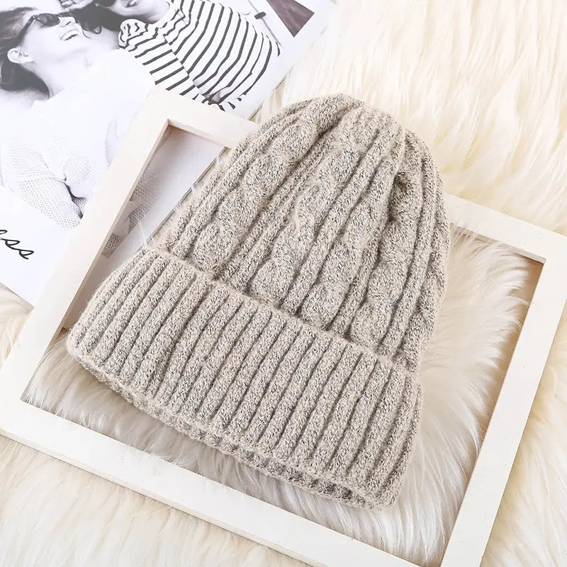 A cozy beige cable knit beanie hat with a ribbed brim made from soft yarn and fleece lined for winter warmth.