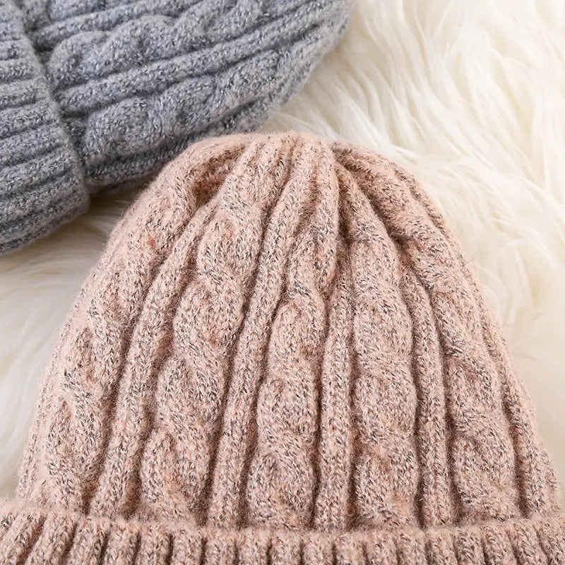 A cozy blush pink cable knit beanie hat with a ribbed brim and fleece lining designed for winter warmth.
