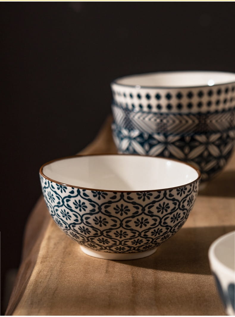A ceramic bowl with a white interior and an exterior decorated with intricate blue floral patterns and a subtle brown rim from a 5 piece Japanese floral porcelain set.