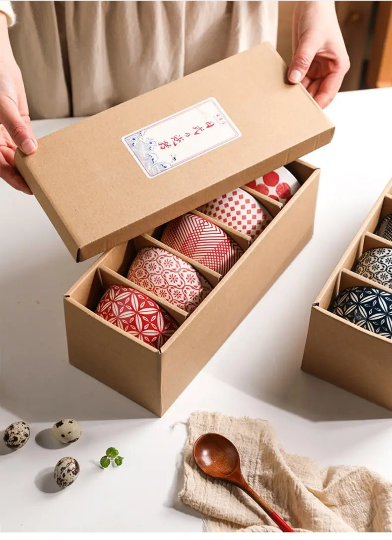 A set of five intricately patterned red white and blue ceramic bowls made of Japanese floral porcelain nestled inside a rustic brown cardboard gift box.