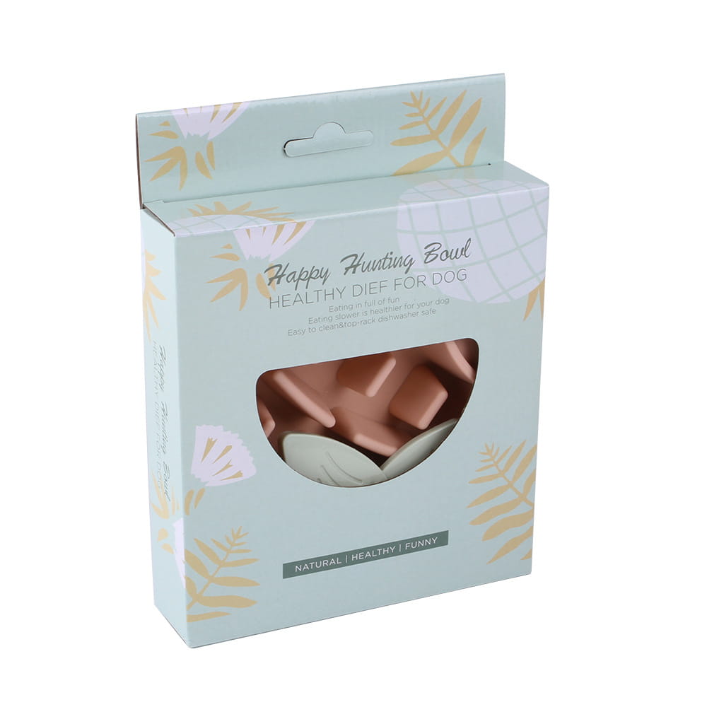 Una caja de cartón color menta pastel con hojas doradas y patrones florales blancos, con una ventana transparente que muestra en su interior cuencos de comida para mascotas de plástico de silicona color rosa con forma de piña para alimentación lenta