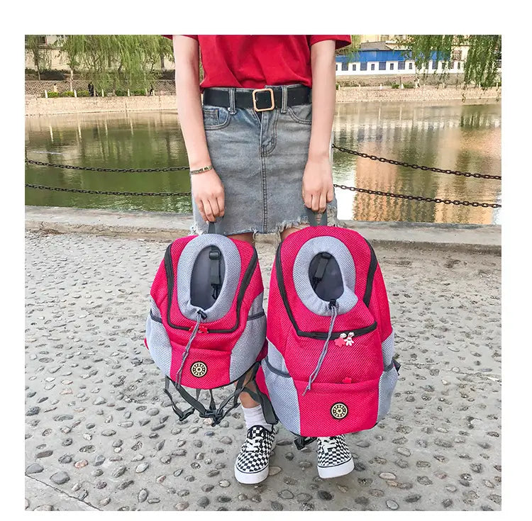 Breathable mesh pet carrier backpack in pink and gray with mesh sides black straps and a circular gold emblem on the front.