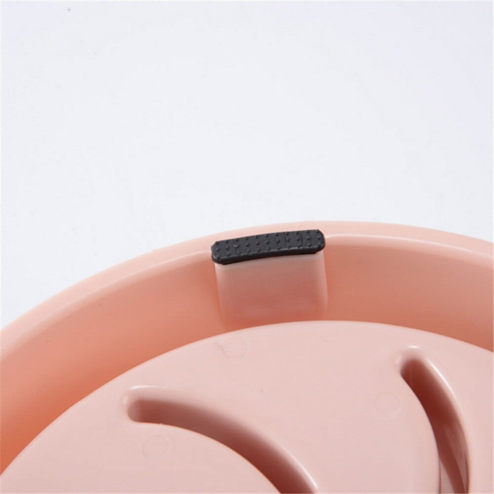 Pink plastic slow feeder dog bowl with a black textured footpad designed as an anti choke dish for pets.