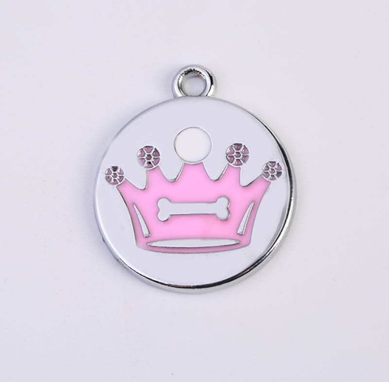 A round silver-toned enamel pet ID tag from the crown enamel pet ID tag 5 pack featuring a pink crown with rhinestones and a white bone design at the center.