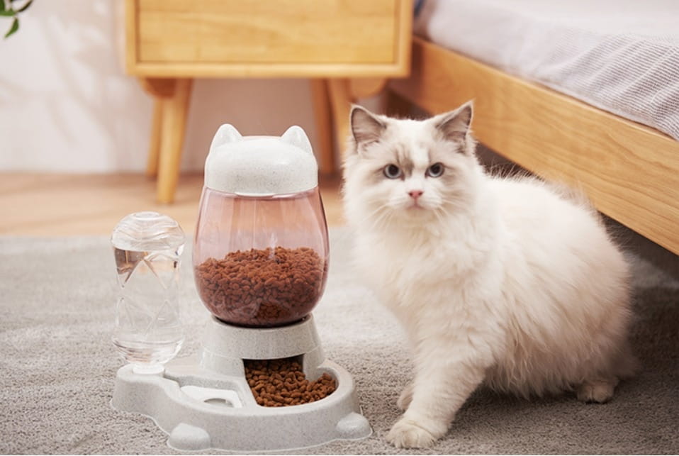 White cat-shaped automatic pet feeder with transparent bowl filled with brown kibble and an attached water dispenser for gravity pet watering station.