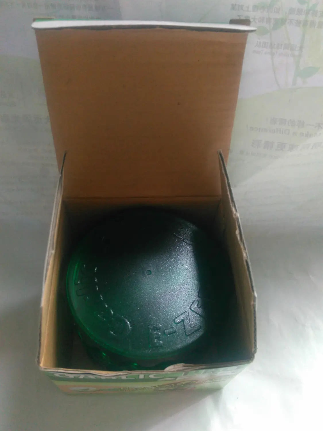 a dark green round soap bar with embossed patterns inside a cardboard box shown alongside the garlic pro manual grinder and peeler kitchen tool