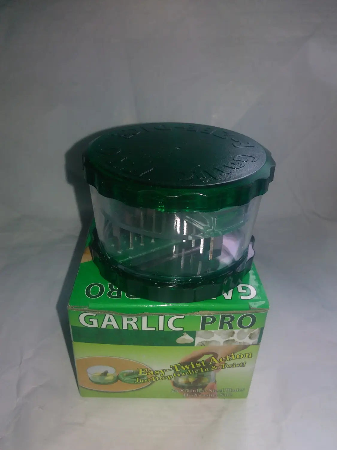 Green plastic garlic pro manual grinder and peeler kitchen tool with a clear central chamber and ridged lid designed for efficient garlic pressing.