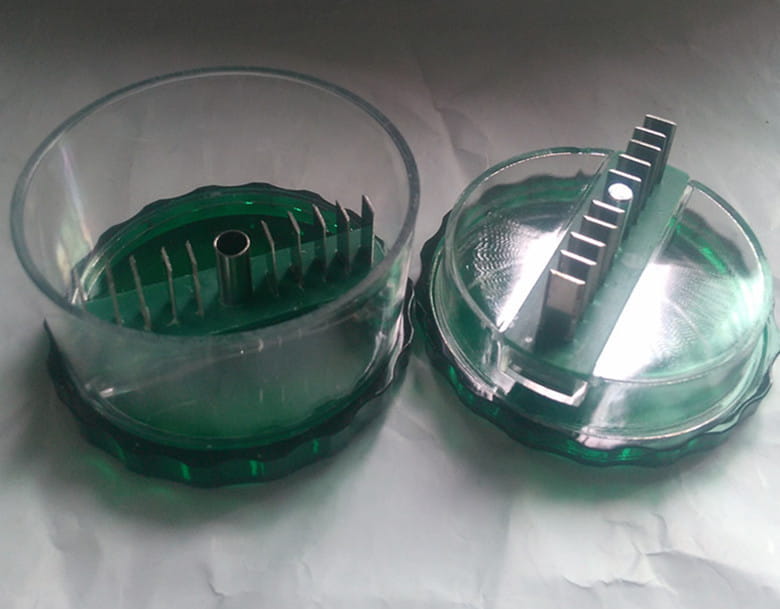 Green plastic garlic pro manual grinder and peeler kitchen tool with clear acrylic lid and metal grinding components.