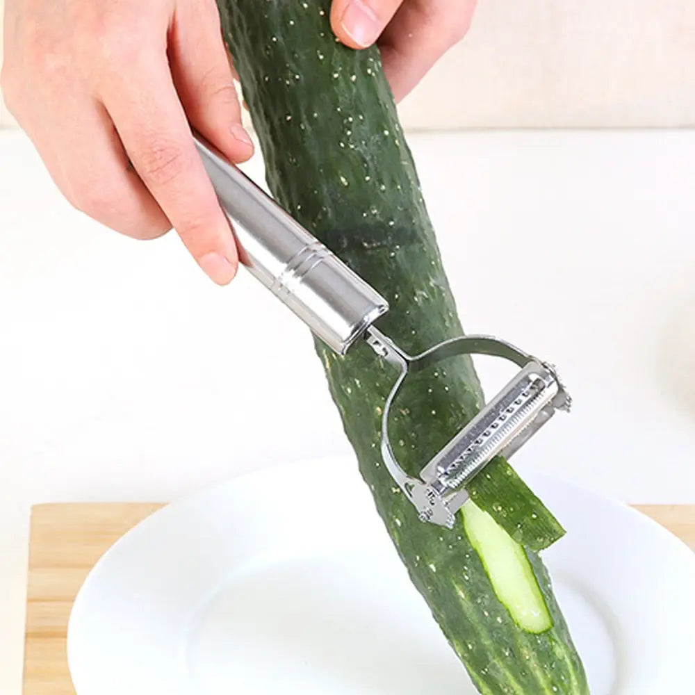 Silver stainless steel 2 in 1 potato peeler and julienne grater with a curved handle and sharp ridged blade peeling a green cucumber.