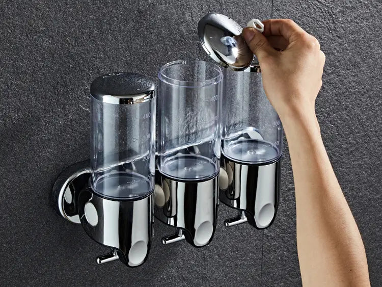 Chrome finished wall mounted soap dispenser triple unit with clear plastic bodies and white caps for bathroom or kitchen use.