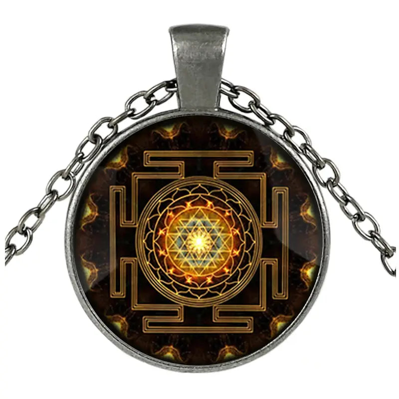 Silver-toned pendant necklace featuring a circular glass cabochon with an intricate golden Sri Yantra design on a dark background suspended from a matching chain.