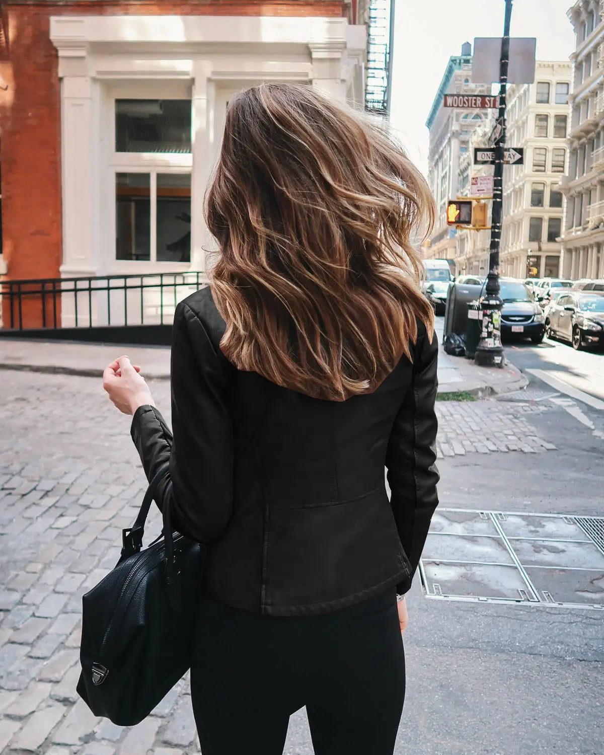 Black leather Prada handbag with a triangular logo on the front paired with a faux leather bomber jacket fitted zip up coat.