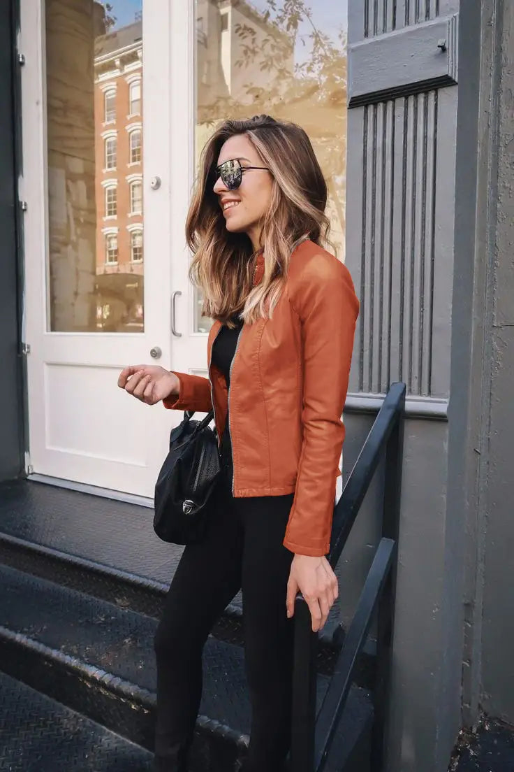 A sleek rust-orange faux leather moto jacket featuring a classic zip-up front and subtle stitching details.