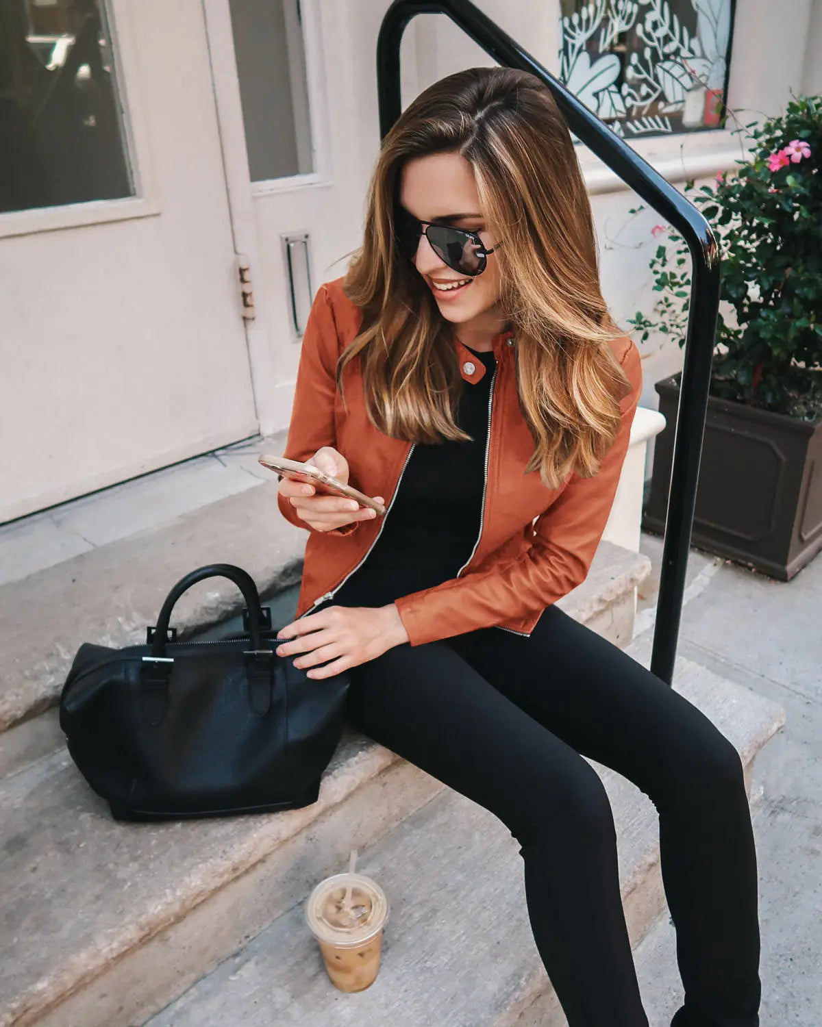 Black leather handbag with structured shape and top handle paired with a faux leather bomber jacket fitted zip up coat.