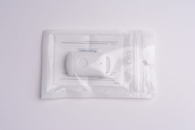White plastic smart bluetooth tracker tag with circular button and small hole for keys pets and kids in clear packaging.