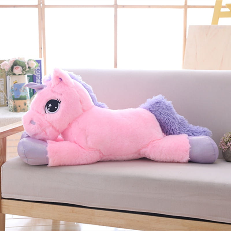 A plush pink unicorn toy with a purple mane and tail lying on its side made of soft stuffed material.