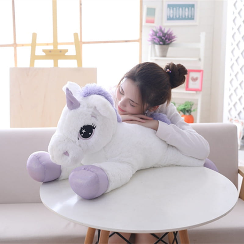 A soft plush unicorn toy in white with lavender accents and large expressive eyes designed as a pink and purple stuffed animal.