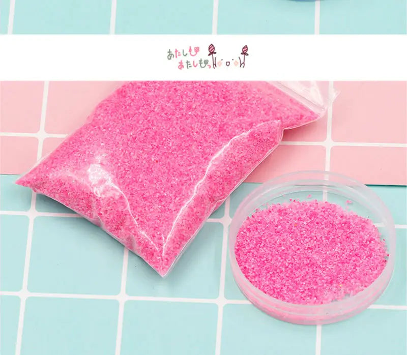 透明なプラスチック袋に入った、ピンクのきらめく撥水・防水の魔法の砂。少しこぼれて透明な丸形の容器に入っており、工作用の子ども向け玩具です