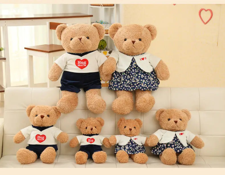 Un peluche de oso de peluche de 55 cm que lleva una camisa blanca de punto con un corazón rojo y el texto «abrázame», y shorts de color azul marino.