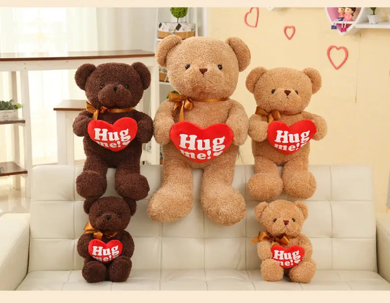 Cuatro peluches de osos de peluche marrones y tostados con texturas de pelaje suave, con suéteres de punto; cada uno sostiene una almohadilla con forma de corazón rojo con el texto «abrázame», atada con cintas doradas y con medidas de 55 cm.