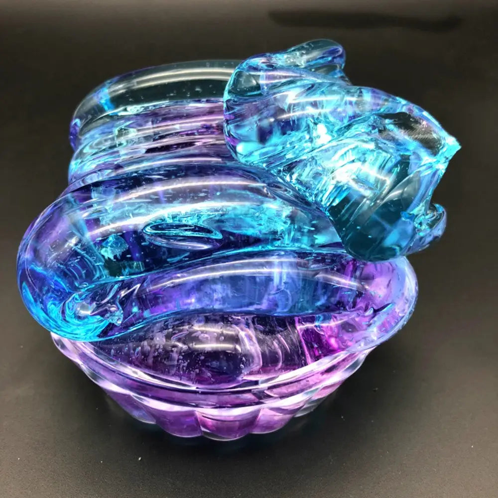 A translucent blue and purple glass sculpture of a coiled snake with intricate ridges featured in the gradient crystal mud slime blue and purple putty toy.