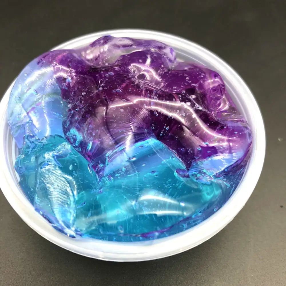 Vibrant blue and purple gradient crystal mud slime with a glossy translucent texture sits in a white plastic container as a putty toy.