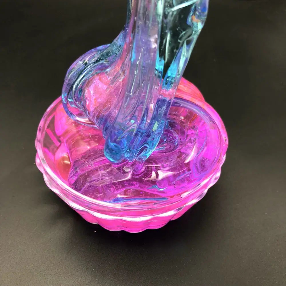 A vibrant translucent gradient crystal mud slime in pink and blue being stretched over a matching pink glass bowl.