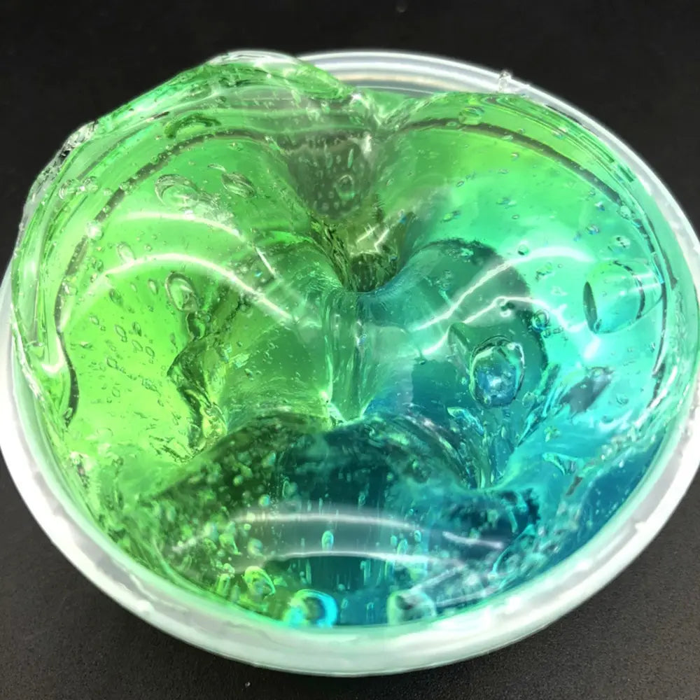 A vibrant green and blue gradient crystal mud slime putty toy with a glossy translucent texture contained in a clear plastic cup.