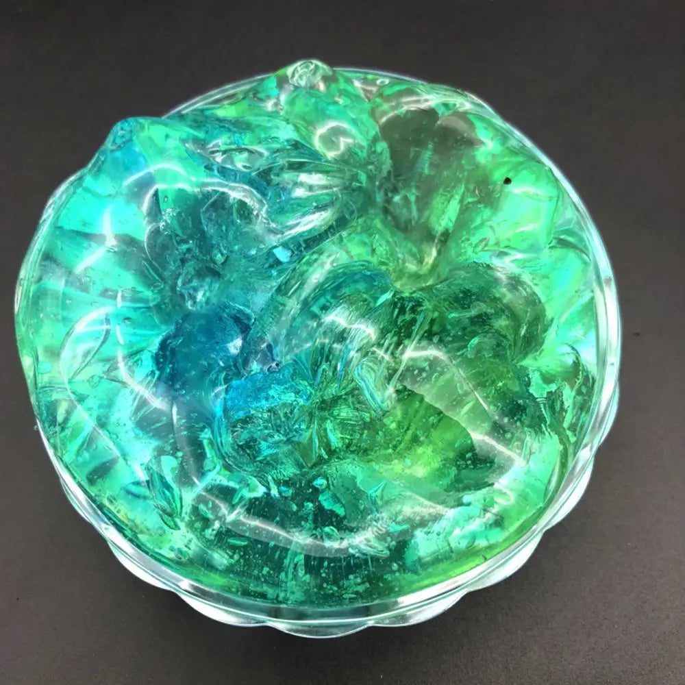 a translucent swirling green and blue gelatinous gradient crystal mud slime putty toy contained within a clear glass bowl