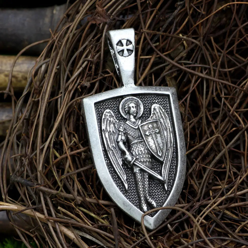 Silver shield-shaped pendant featuring an intricately engraved Saint Michael archangel in armor with sword shield detailed wings and halos on a braided cord necklace.