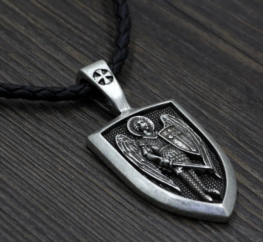 Silver shield-shaped pendant featuring an engraved winged angel holding a sword and shield on a black braided cord in a Saint Michael Archangel shield pendant necklace.