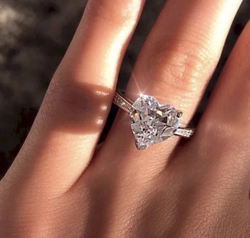 A heart shaped zircon engagement ring with a sparkling diamond set in a sleek white gold plated band featuring subtle pave detailing.