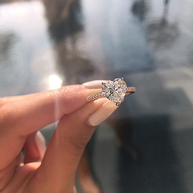 A rose gold heart shaped zircon engagement ring with a diamond center and smaller diamonds along the band in white gold plating.