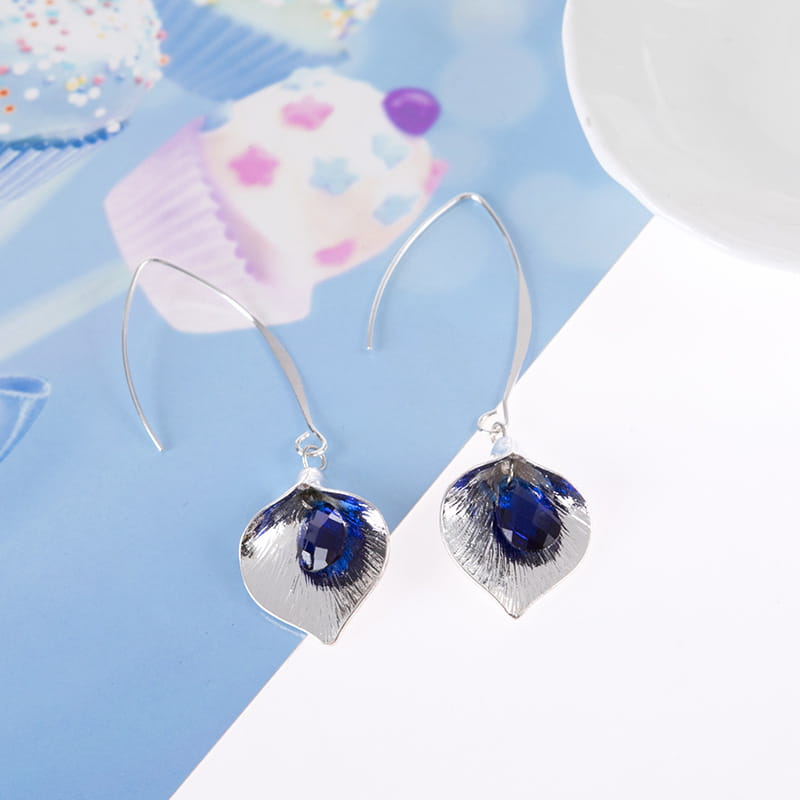 Boucles d’oreilles pendantes en cristal d’orchidée argentée texturée, ornées d’un motif en forme de feuille d’argent, avec des pierres facettées bleu profond au centre.