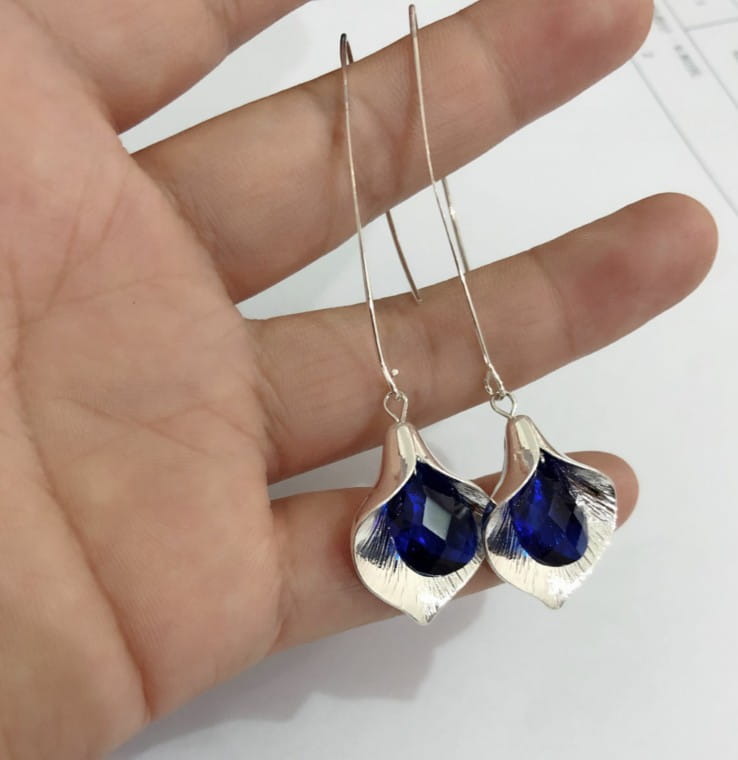 Boucles d’oreilles pendantes en cristal d’orchidée argentée texturée, avec des pierres facettées bleu profond montées dans un travail métallique en forme de feuille.