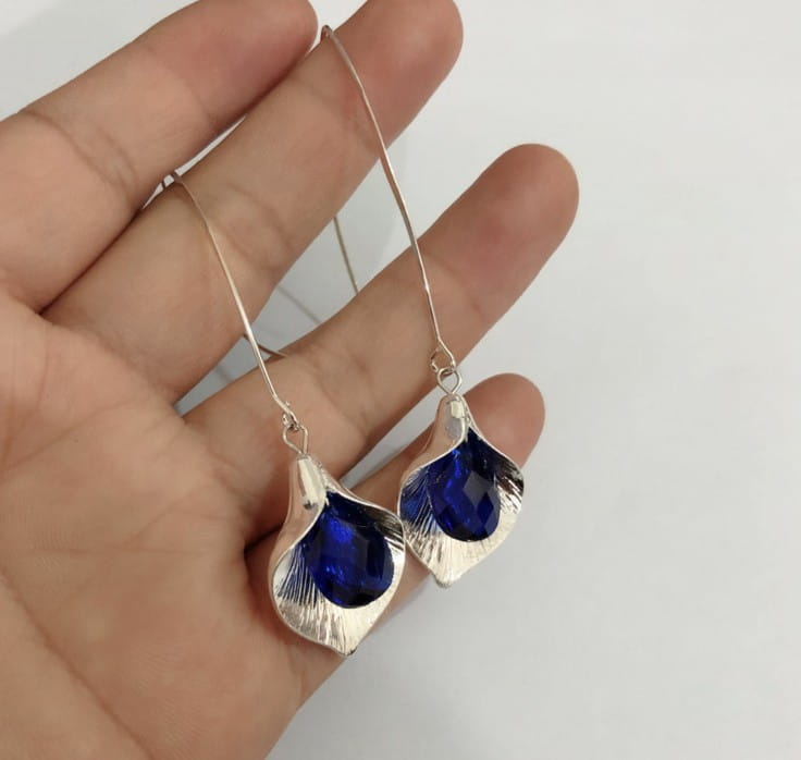 Boucles d’oreilles pendantes en cristal d’orchidée argentée texturée élégantes, avec un motif en forme de feuille et des pierres facettées bleu profond.