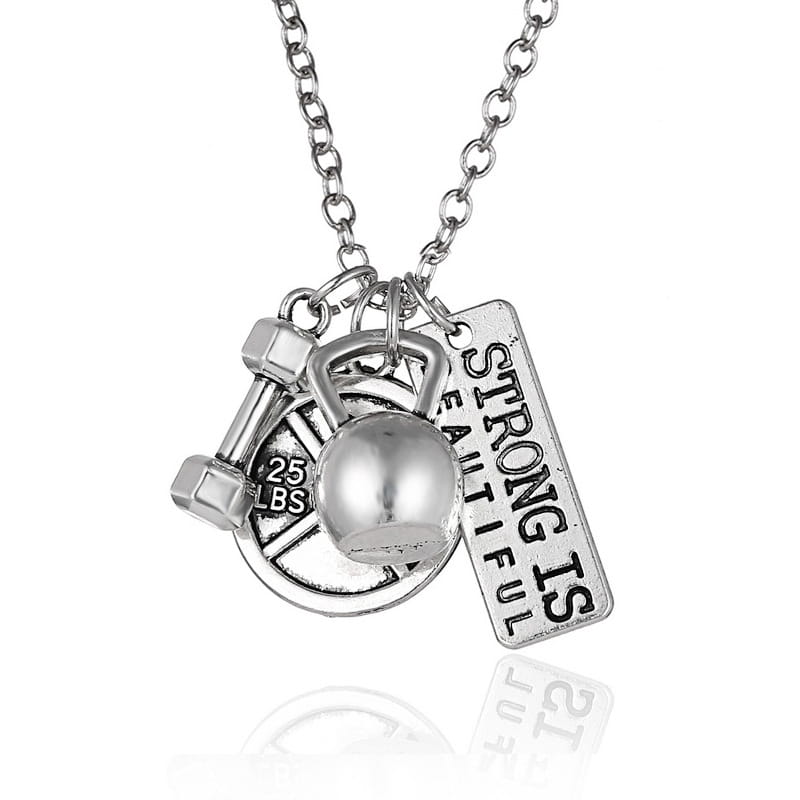 Silver-toned inspirational fitness pendant necklace with gym charms including a kettlebell dumbbell weight plate and an engraved strong is beautiful tag.