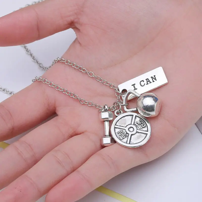 Silver-toned inspirational fitness pendant necklace featuring gym charms including a weight plate, dumbbell, bell, and i can charm.