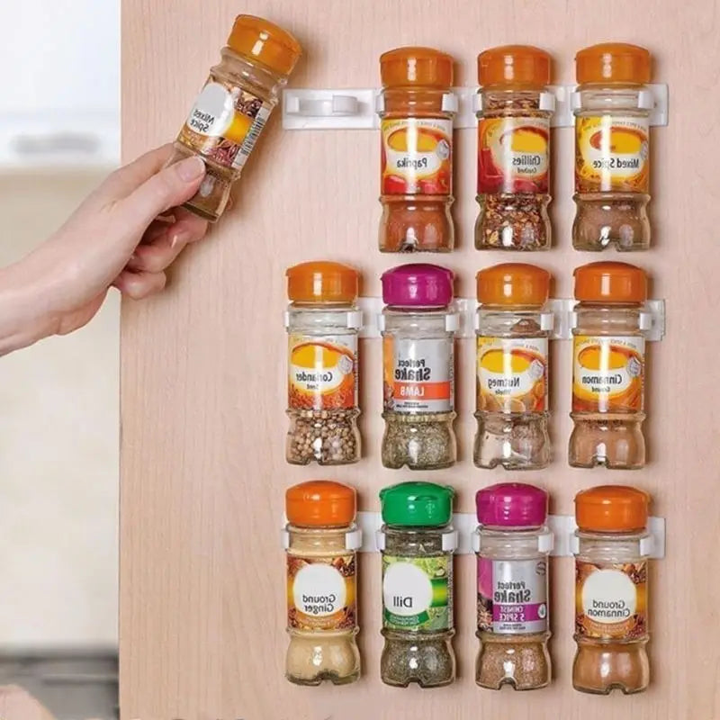 A set of clear glass spice jars with colorful orange purple and green caps neatly arranged on a white magnetic wall mount spice rack organizer with adhesive clips.