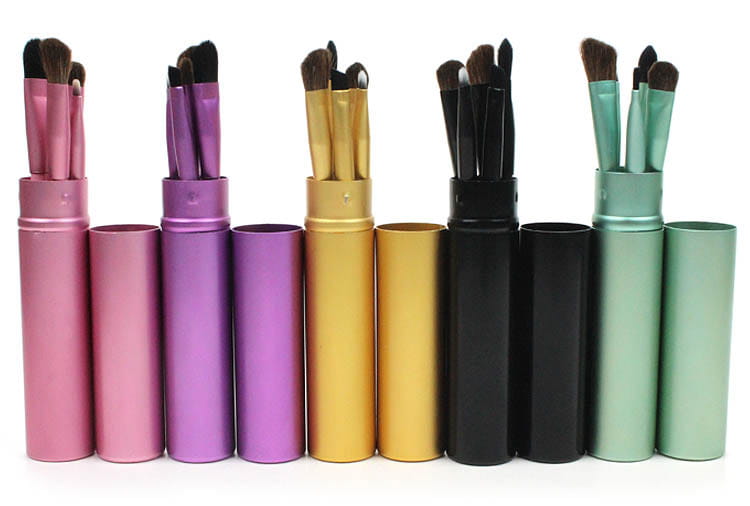 Set of five colorful metallic cylindrical brush cases each holding multiple makeup brushes with matching colored handles and bristles for travel eye makeup use.