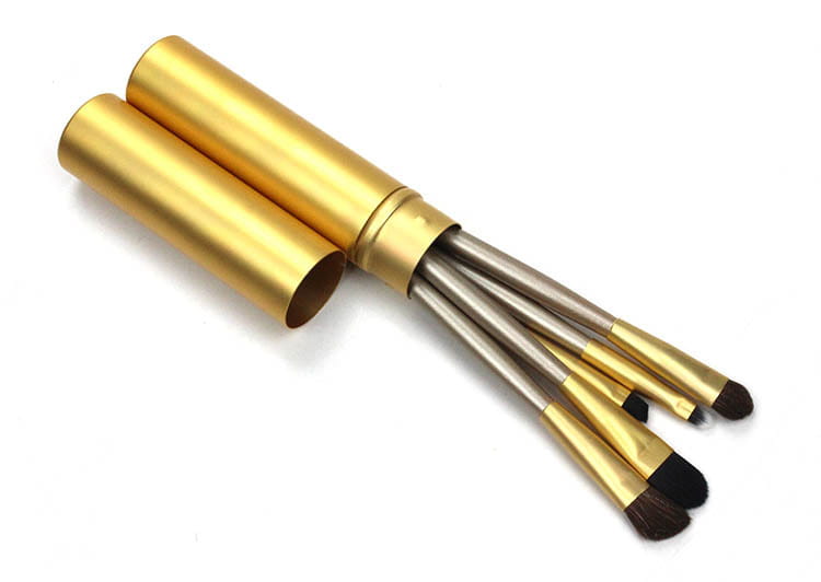 Golden cylindrical case holding five makeup brushes with metallic handles and black bristles in a travel eye makeup brush set with portable case.