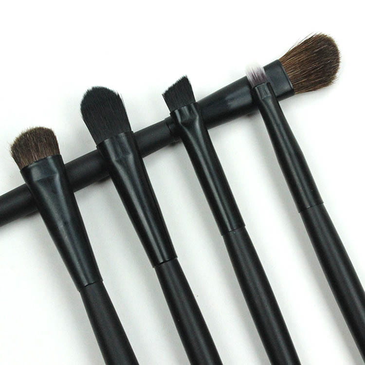 Set of five black-handled travel eye makeup brushes with dense dark brown bristles arranged in a row designed for precise application and portability