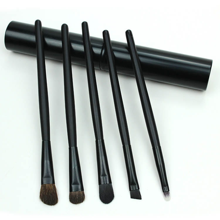 Set of six black synthetic travel eye makeup brushes with varying head shapes and sizes neatly arranged beside a matching cylindrical portable case.